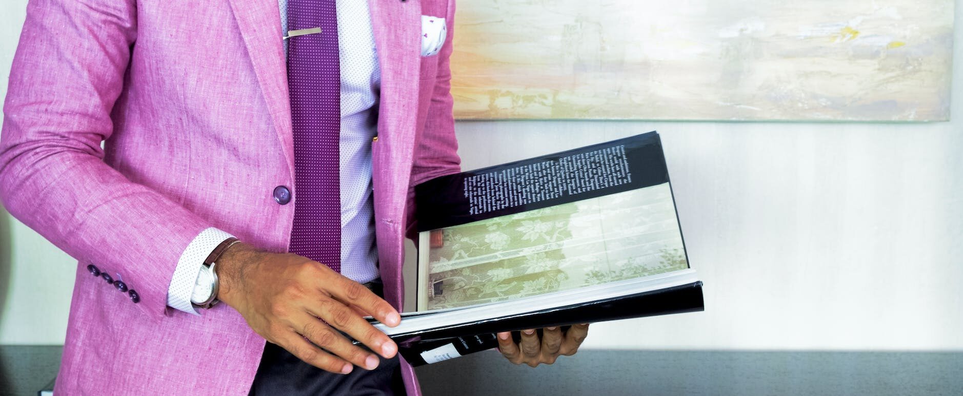 man in pink suit jacket holding book